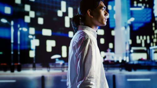 Side view of young woman looking away while standing in city at night