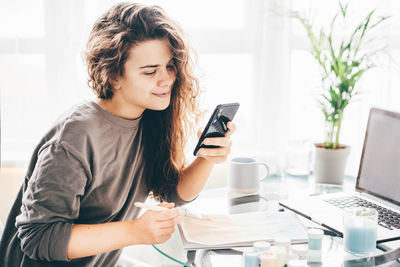 Young woman using mobile phone while sitting at home