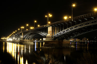 Illuminated bridge over river against sky at night