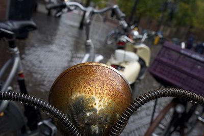 Close-up of rusty bicycle headlight on wet footpath