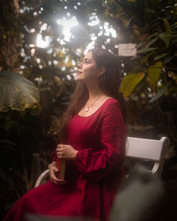 Portrait of a woman in a red dress with a book, sitting on the bench in nature.