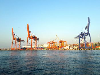 Cranes at commercial dock against clear blue sky