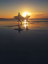 Silhouette men with surfboards running at beach during sunset