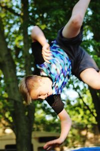 Tilt image of teenage boy jumping against trees