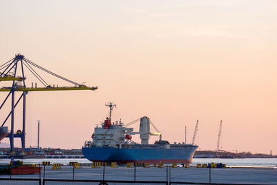 Cranes at commercial dock against sky during sunset