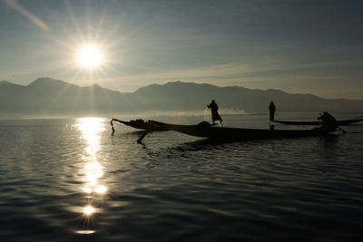 Silhouette people on boat in lake against sky during sunset