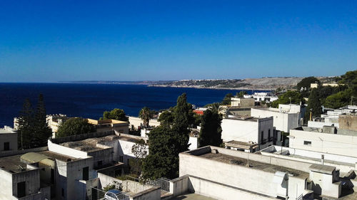 High angle view of townscape by sea against clear blue sky