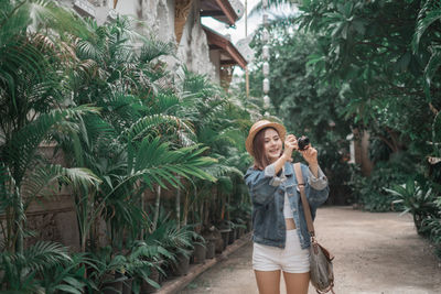 Full length of young woman standing on footpath against trees