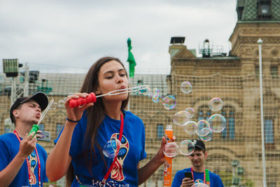 Young woman with bubbles standing against buildings