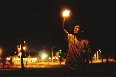 Man holding illuminated light against sky at night