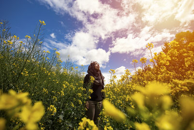 Young woman standing amidst yellow flowering plants against sky