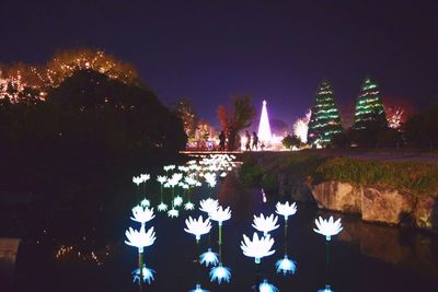 Illuminated city by lake against clear sky at night