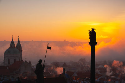 Silhouette people by buildings against sky during sunset