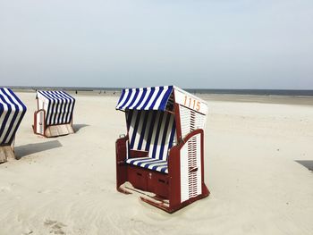 Hooded chairs on beach against sky