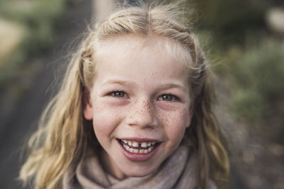 Close-up portrait of happy girl with blond hair standing in forest