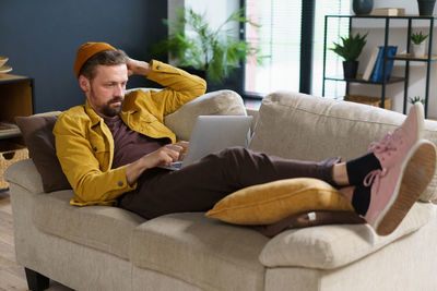 Side view of woman using digital tablet while sitting on sofa at home