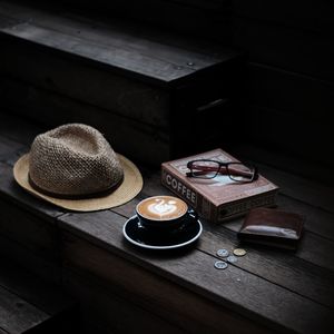 High angle view of coffee with straw hat with book and wallet on wooden table