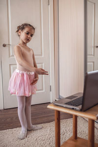 Pretty young ballerina practicing classic choreography during online class, social distance