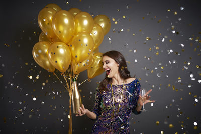 Happy woman holding balloons while standing against gray background