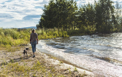 Rear view of young woman walking along  lake shore with mixed breed dog travel and hiking with pets