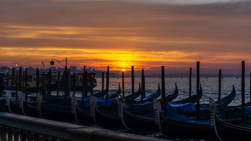 Boats moored in sea against cloudy sky during sunset