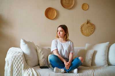 Stressed young woman sitting on sofa in casual clothes, worrying about problems