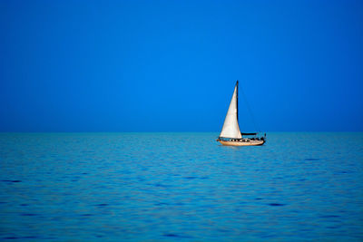 Sailboat sailing in sea against clear blue sky