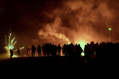 Silhouette people looking at firework display against sky at night