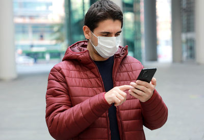 Man wearing mask using smart phone while standing outdoors