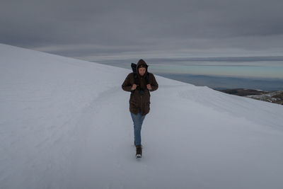 Man walking on snow covered landscape against sky