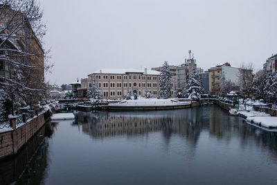 Reflection of buildings in city against clear sky during winter