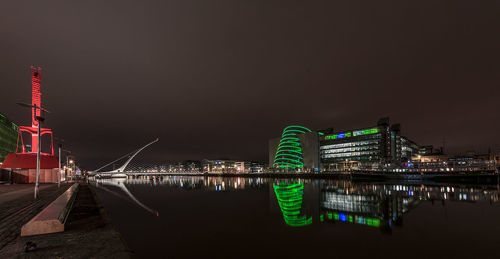 Reflection of illuminated buildings in river against clear sky at night