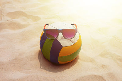 Sunglasses with colorful ball at sandy beach on sunny day
