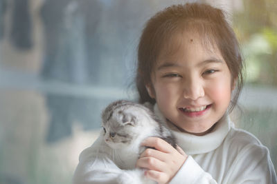 Portrait of happy girl with scottish fold cat sitting by window at home