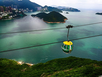 Overhead cable car by sea against mountains