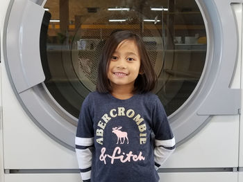 Portrait of smiling girl standing against washing machine