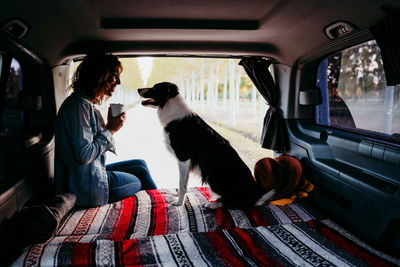 Woman holding mug with dog sitting in camper trailer