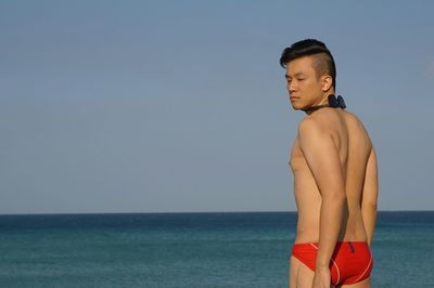 Shirtless man standing at beach against sky