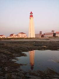 Lighthouse amidst sea and buildings against sky