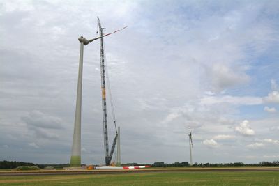 Incomplete windmill by crane against blue sky