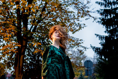 Portrait of young woman with tousled hair standing against trees