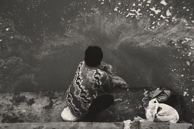 Rear view of people sitting on rock by water