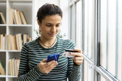 Female entrepreneur paying through credit card while online shopping on mobile phone in office