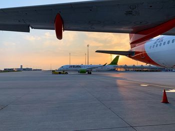 Airplane on airport runway against sky during sunset