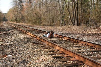 Mature woman photographing while lying on railroad tracks in forest