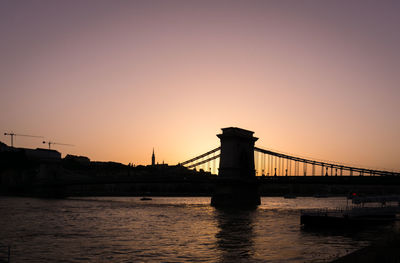 Silhouette bridge over river against sky during sunset