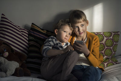 Siblings using mobile phone while sitting on sofa at home
