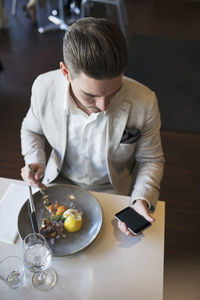 High angle view of businessman using mobile phone while eating lunch at restaurant