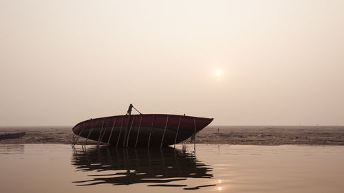 Boat moored on shore against sky during sunset