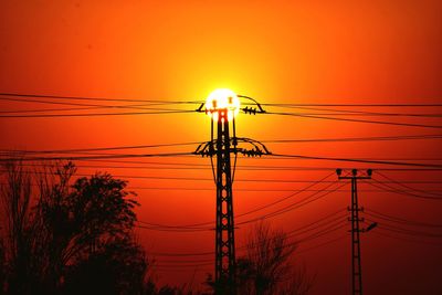 Low angle view of electricity pylon against sky during sunset